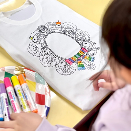 A child is painting T-shirt with colourful markers.