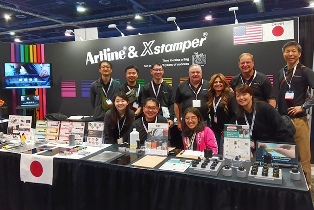 A group photo of the Artline & Xstamper team at the exhibition booth, showcasing various products with an inviting setup.