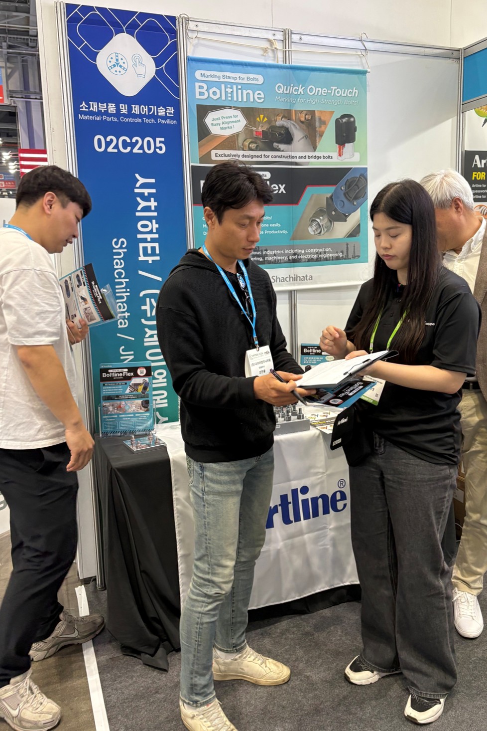 Shachihata staff and visitors are discussing Artline and Boltline products at the booth.