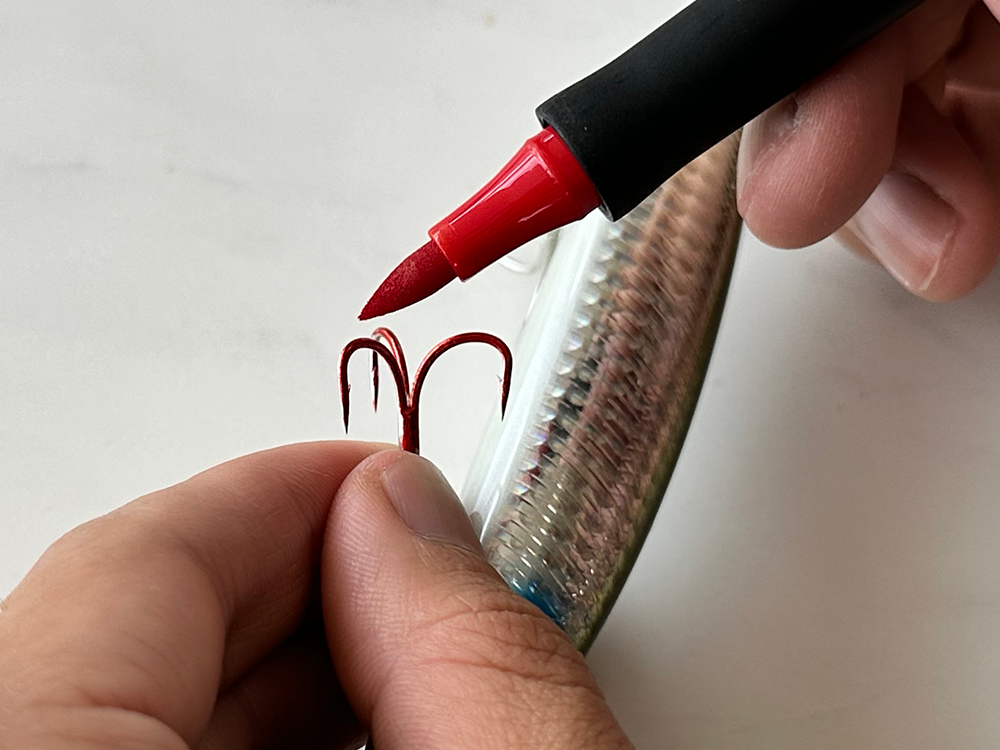 Pintar anzuelo de pesca de metal con marcador de tinta roja.